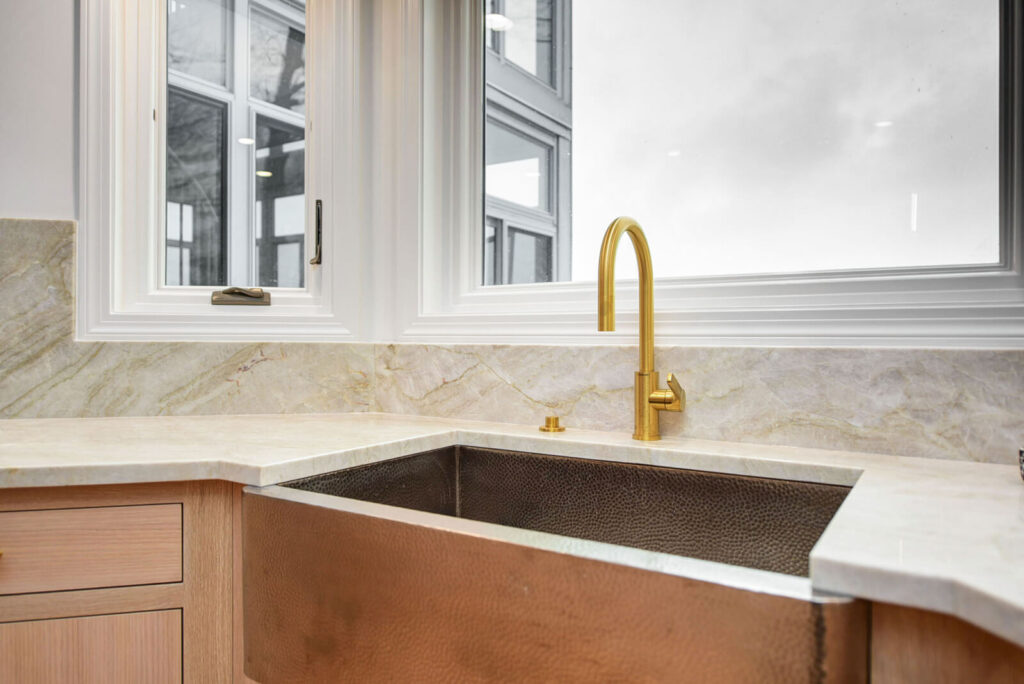 A kitchen sink featuring a gold faucet, positioned beneath a window, showcasing a bright and elegant design.